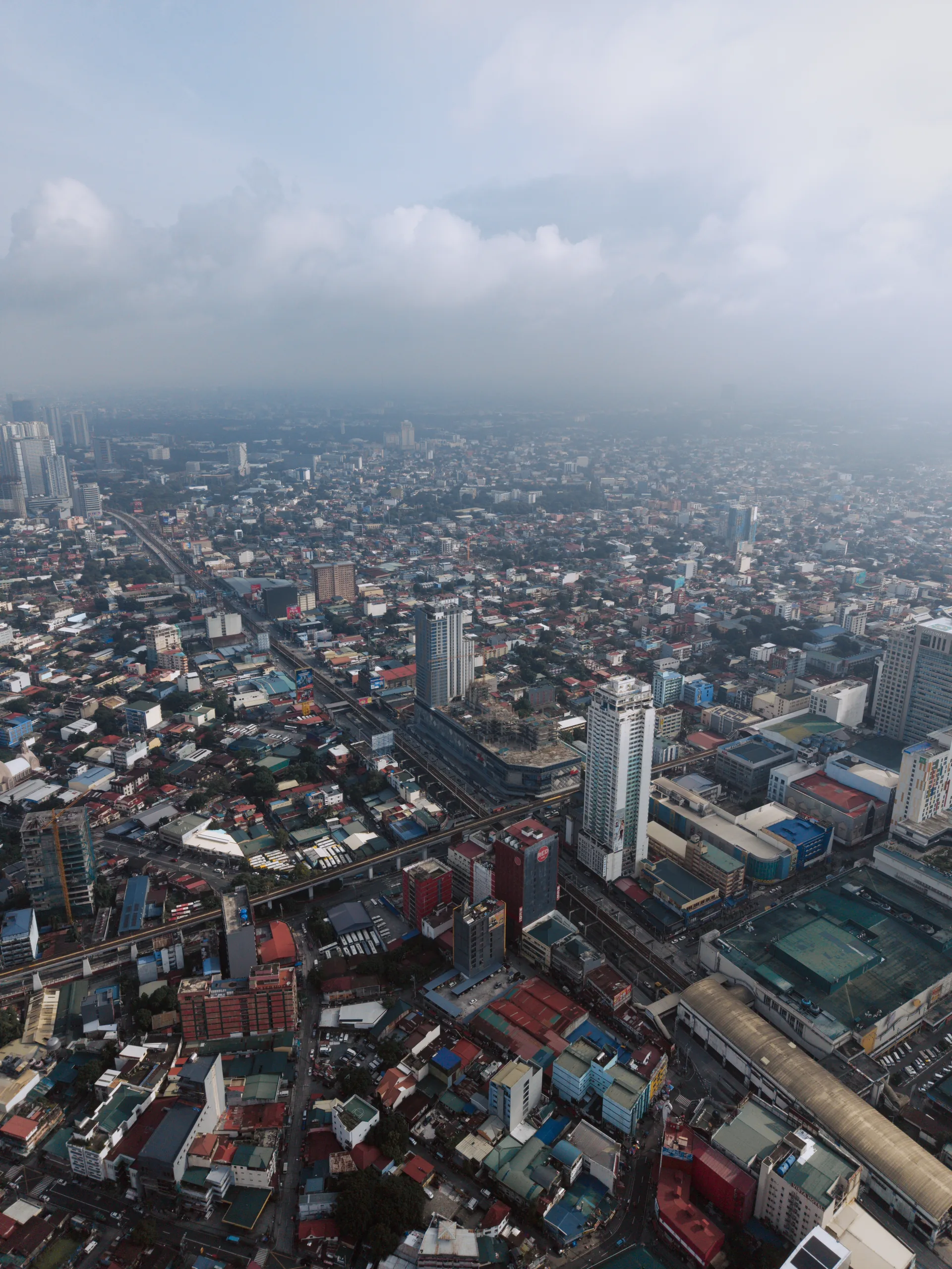 An elevated railway curves through a dense city beneath low white clouds.