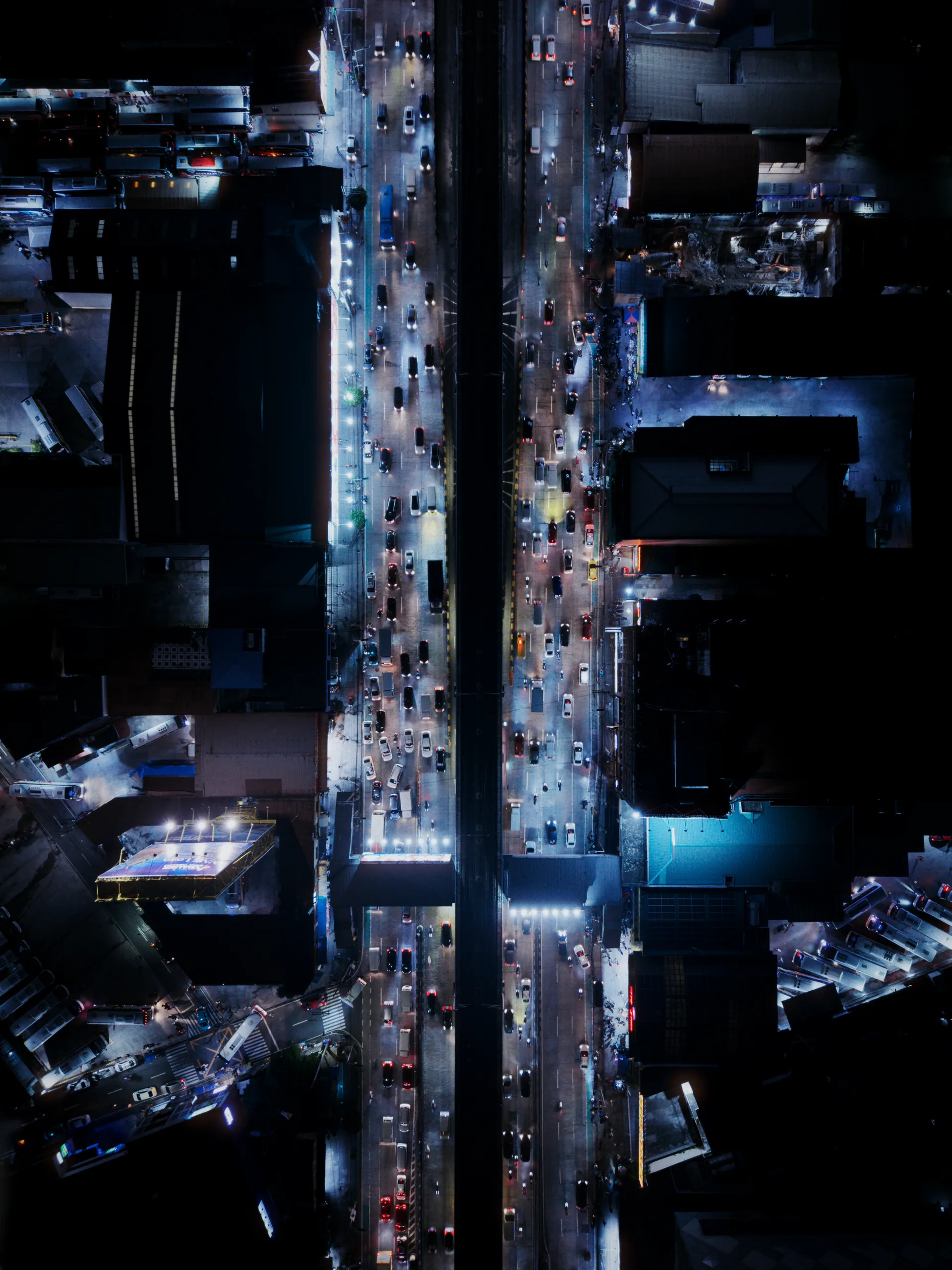 A straight-down aerial photograph of traffic flowing along a brightly lit city road at night.