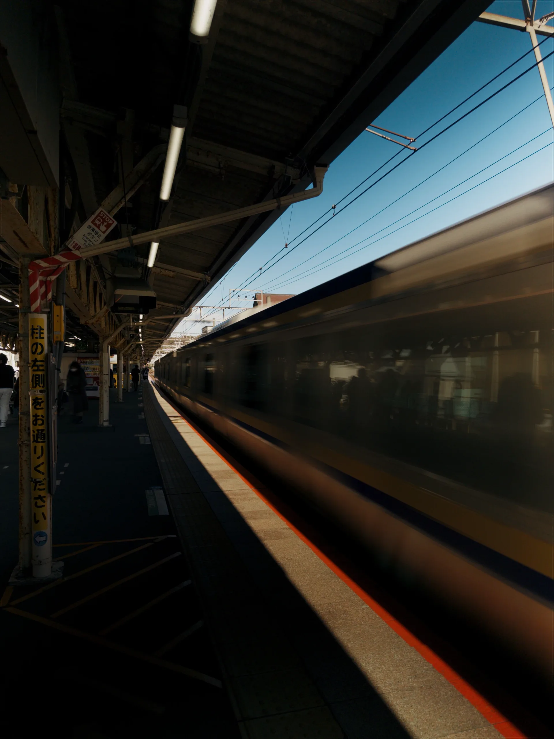 A train blurring past a station platform in Japan.