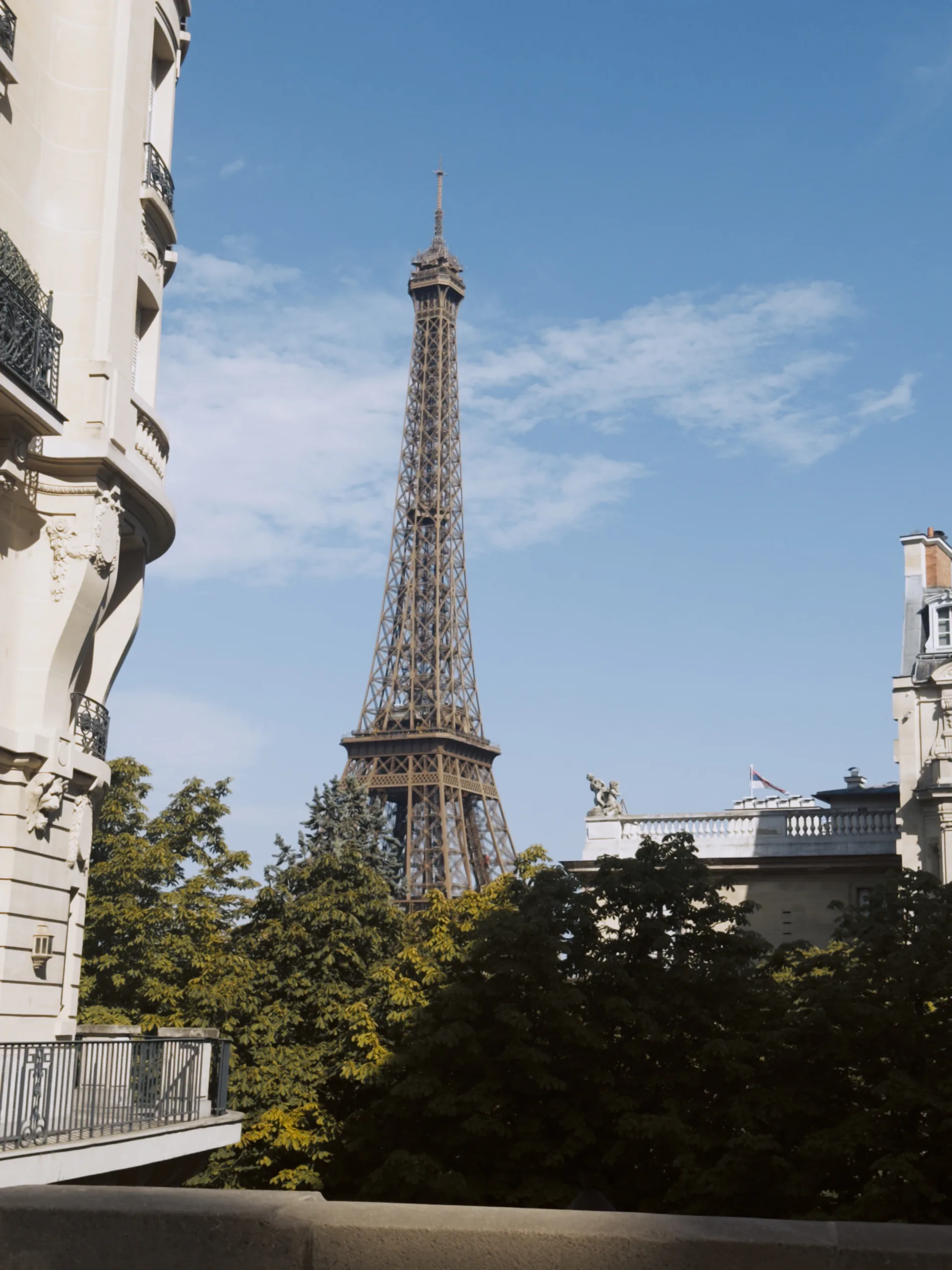 The Eiffel Tower rising between Parisian buildings beneath a blue sky.