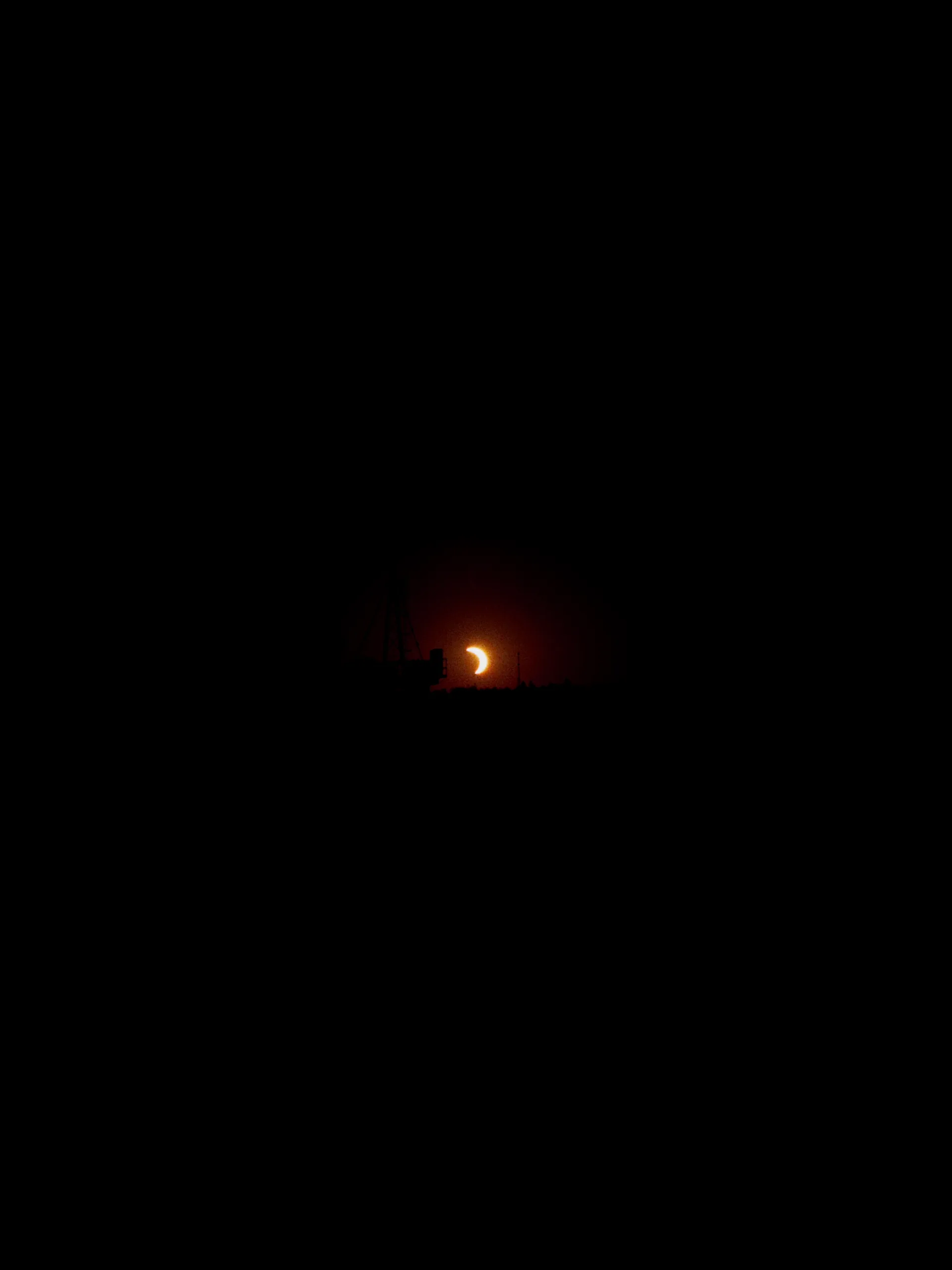 The thin crescent of a partially eclipsed sun setting behind a dark rooftop.